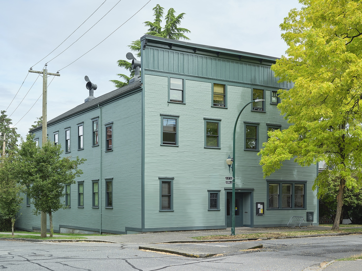 A colour photograph that looks north onto Western Front exterior, a large three story heritage building, with green wooden siding, and a false front façade. 
