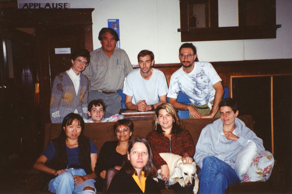 A colour photograph of Western Front staff seated on and standing behind a couch in the Grand Luxe Hall.