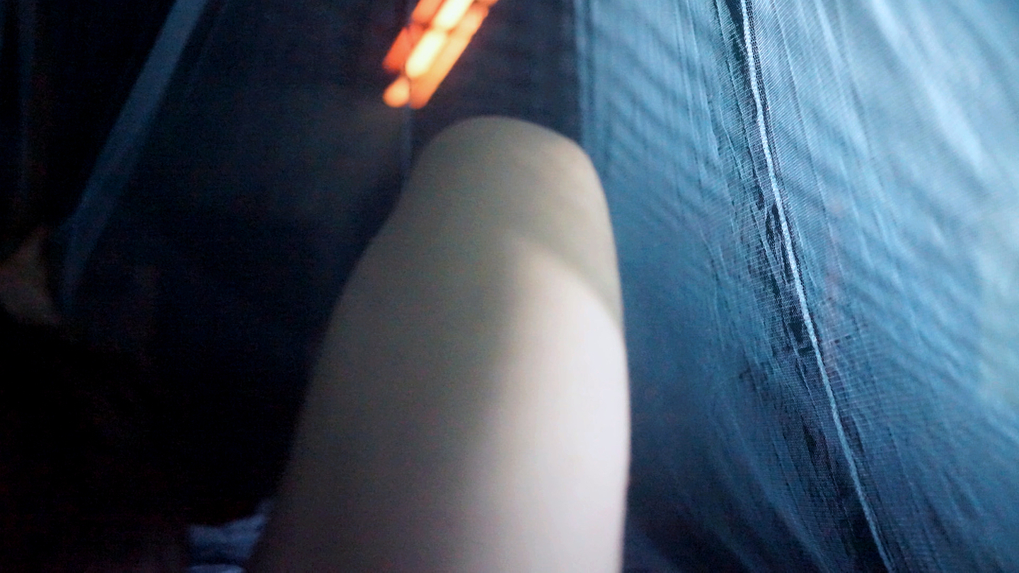 A bare leg bent at the knee is seen under a canopy of blue sheer fabric. 